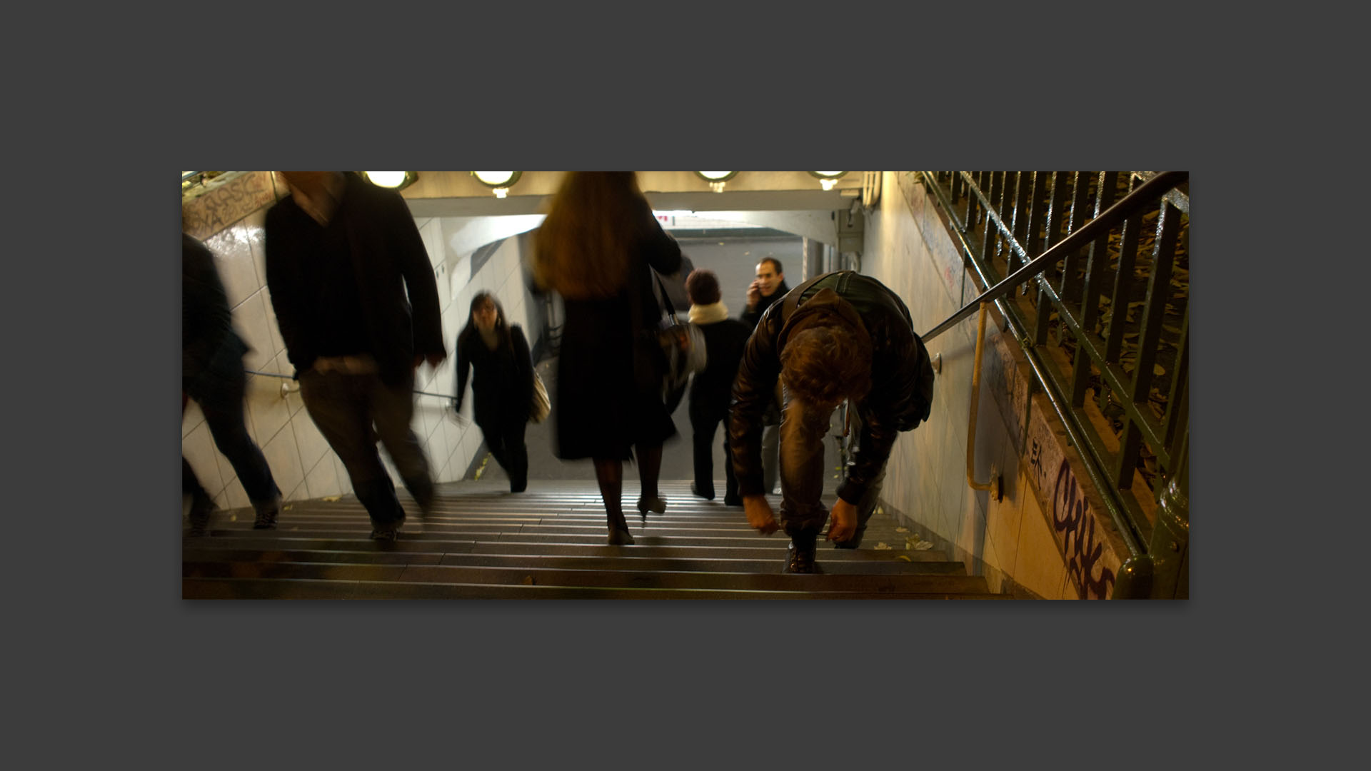 Homme relaçant sa chaussure en sortant de la bouche du métro, au Châtelet, à Paris.