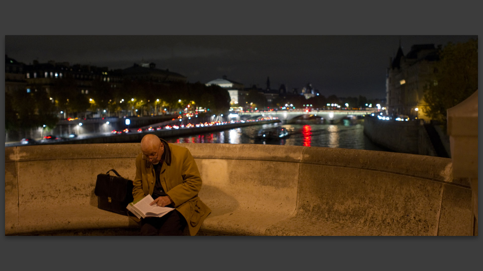 Homme lisant un livre sur un banc de pierre du Pont Neuf, à Paris.