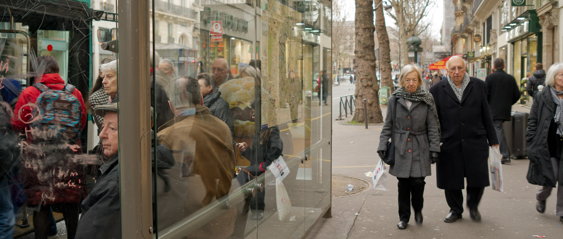 Passants derriere un abribus, boulevard Saint-Germain, à Paris.