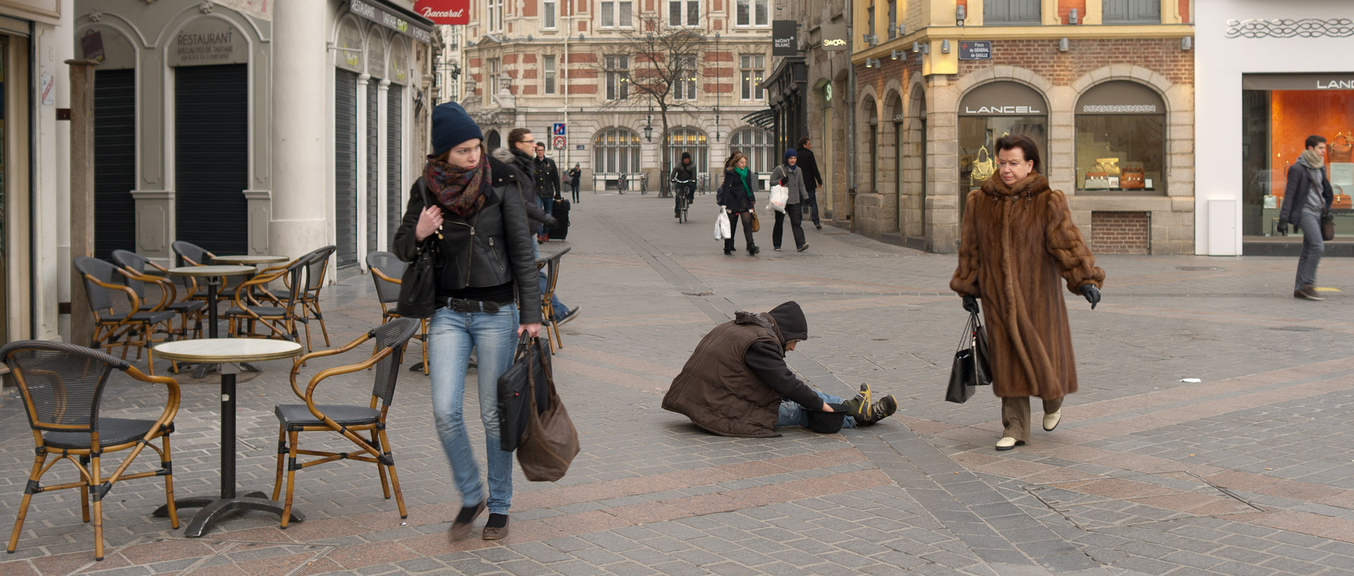 Femme avec un manteau de fourrure passant devant un mendiant, place du Général-de-Gaulle, à Lille.