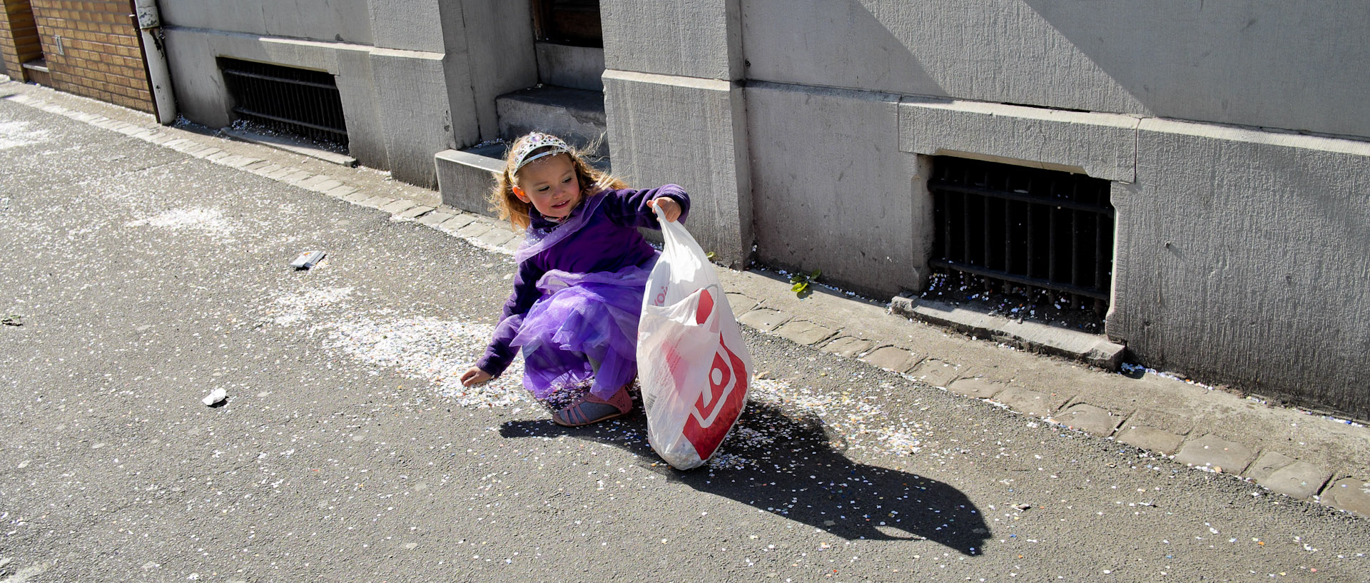 Petite fille costumée ramassant des confettis, rue Carnot, à Wattrelos.