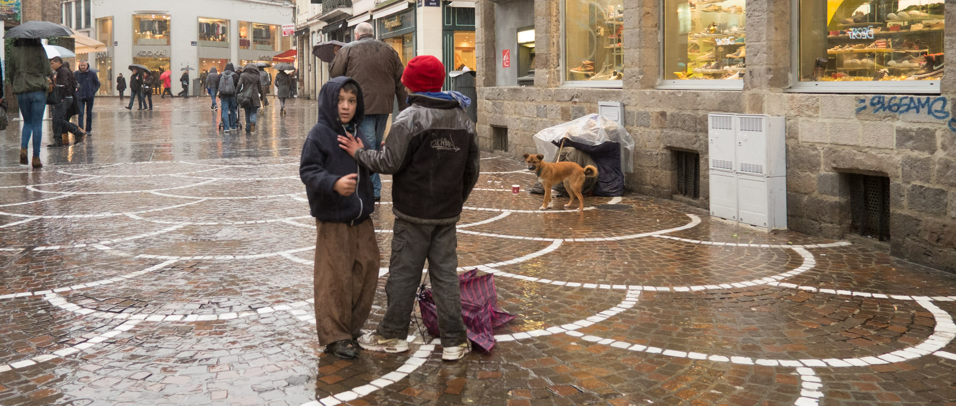 Enfants Roms se disputant un parapluie brisé, devant un mendiant, rue du Secrétaire Arembault, à Lille.
