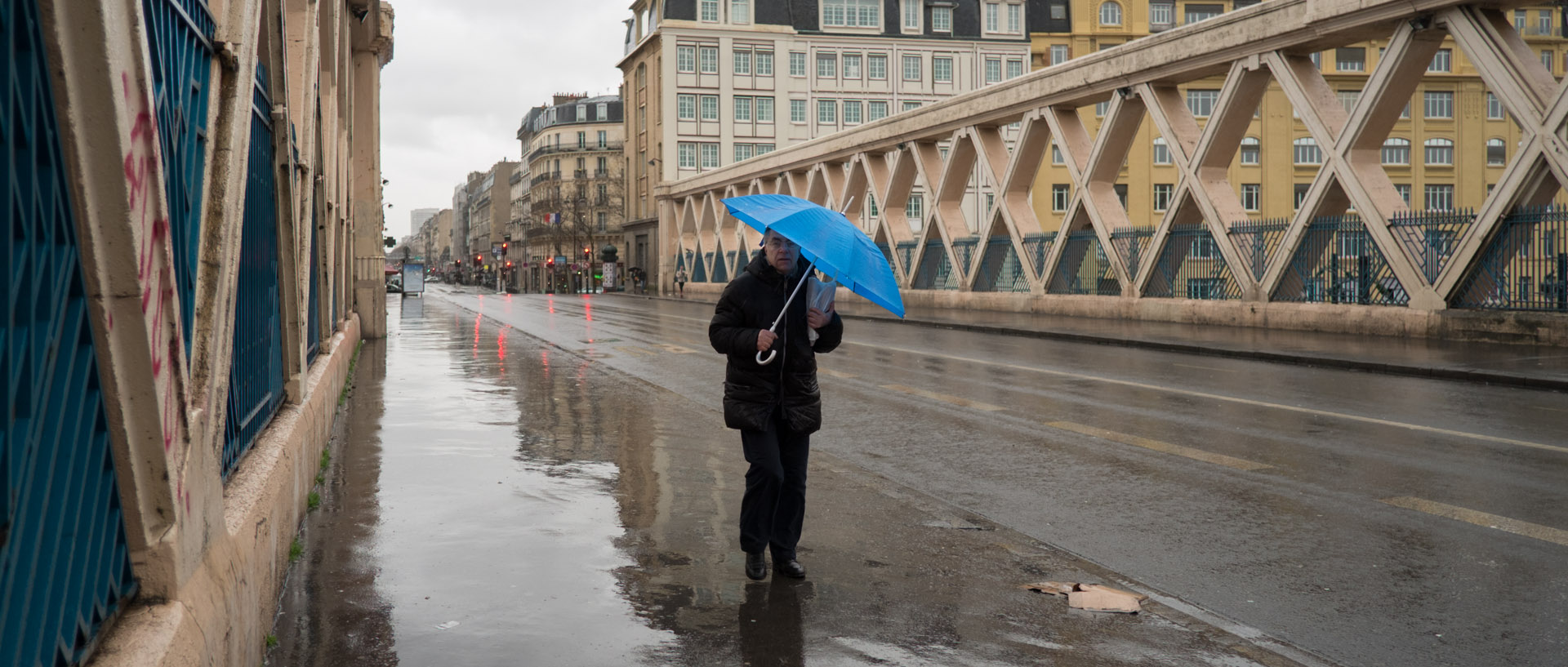 Homme avec un parapluie sur un pont, rue La Fayette, à Paris.