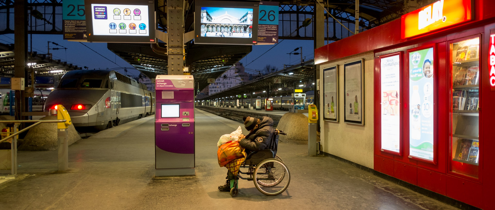 Homme dormant sur un fauteuil roulant, gare de l'Est, à Paris.