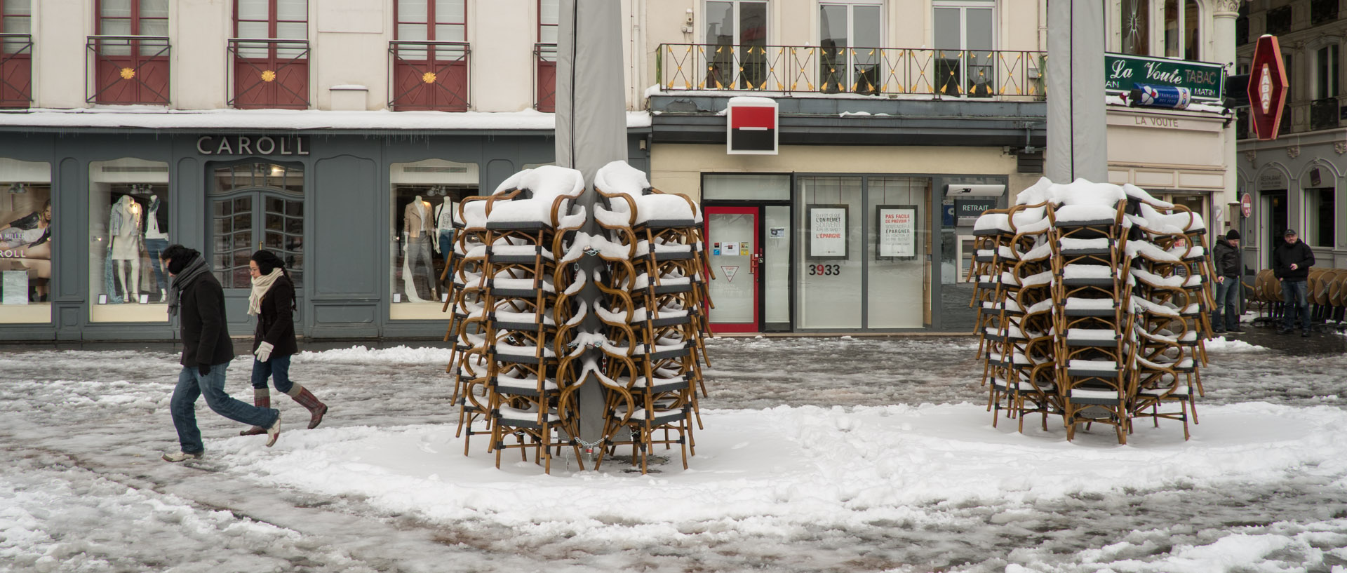 Passants devant des piles de fauteuils sous la neige, place du Général-de-Gaulle, à Lille.