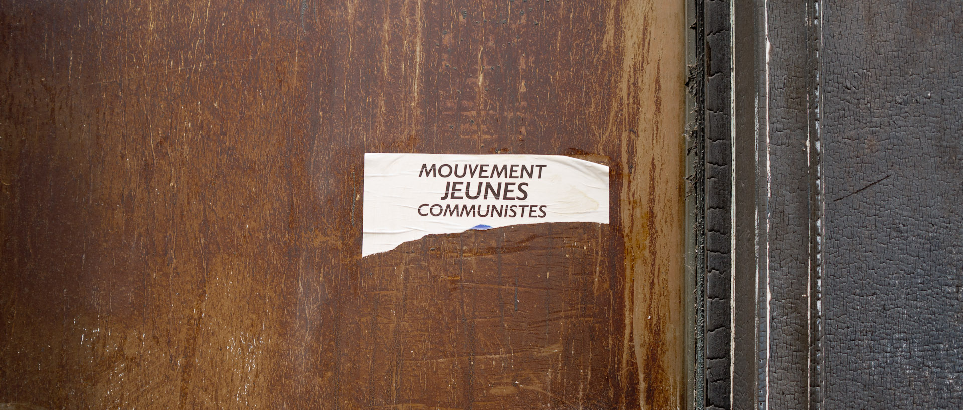 Affichette déchirée du Mouvement des Jeunes Communistes, sur une vieille porte, rue de l'Alouette, à Roubaix.