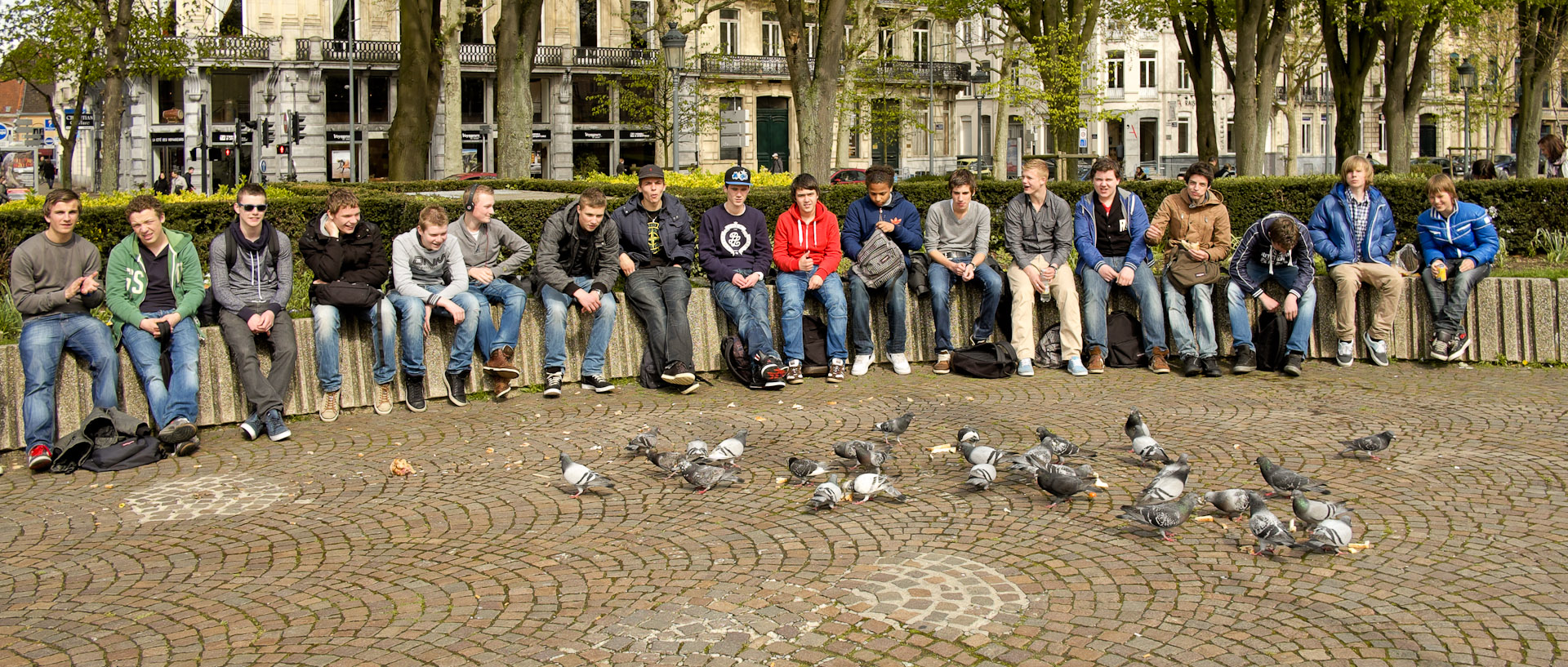Groupe de jeunes assis devant des pigeons, place de la République, à Lille.