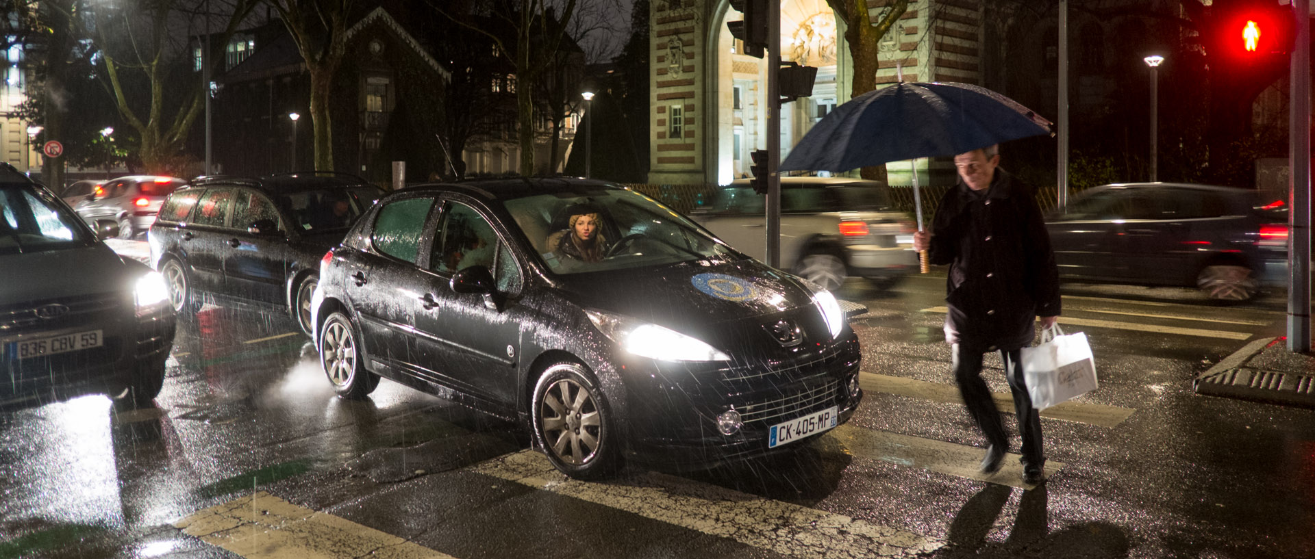 Piéton traversant devant des voitures, sous la pluie, boulevard Vauban, à Lille.